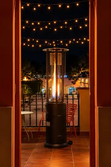 La terraza de Jelou de noche: un calentador encendido, una silla roja y luces colgantes